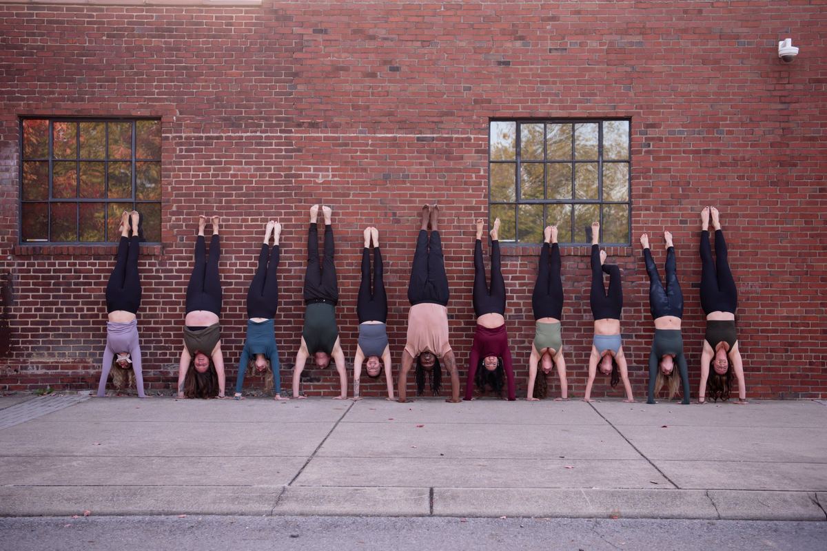 The Donelson Hot Yoga teachers in a row of handstands against a brick wall